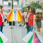 Duas mulheres brancas seguram sacolas coloridas e observam vitrine; Sustentabilidade e ética empresarial contribuem para a percepção do consumidor sobre o valor da marca