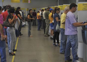 em fila, pessoas aguardam para utilizar caixas eletrônicos em agência bancária