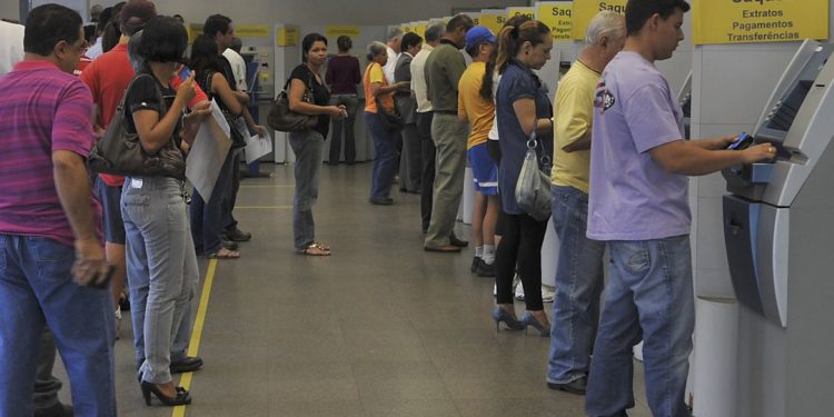 em fila, pessoas aguardam para utilizar caixas eletrônicos em agência bancária