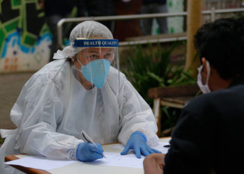 profissional da saúde com máscara e face shield conversa com paciente sentado de frente