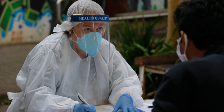 profissional da saúde com máscara e face shield conversa com paciente sentado de frente