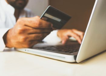 mão masculina segura cartão bancário enquanto utiliza o computador