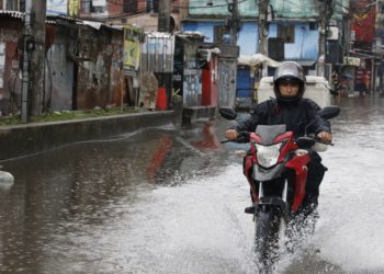 homem atravessa área de enchente com motocicleta