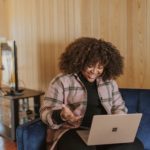 mulher negra utiliza computador sentada no sofá