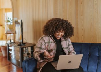 mulher negra utiliza computador sentada no sofá