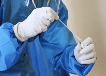 profissional da saúde com luvas e avental azul manueia teste swab