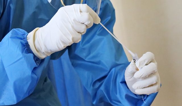 profissional da saúde com luvas e avental azul manueia teste swab