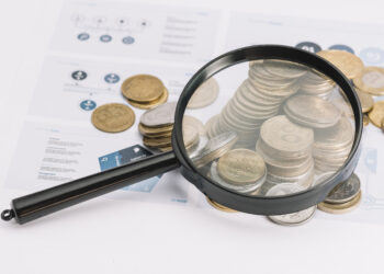 lupa sobre moedas caídas para representar transparência salarial