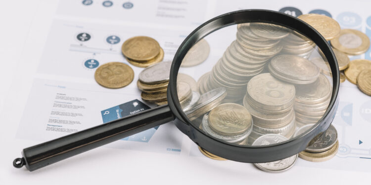 lupa sobre moedas caídas para representar transparência salarial