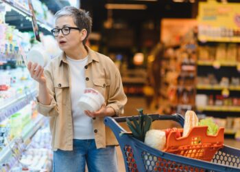 Pessoa analisando diferentes opções de alimentos saudáveis e indulgentes em um supermercado, ilustrando a atenção visual nas escolhas alimentares.