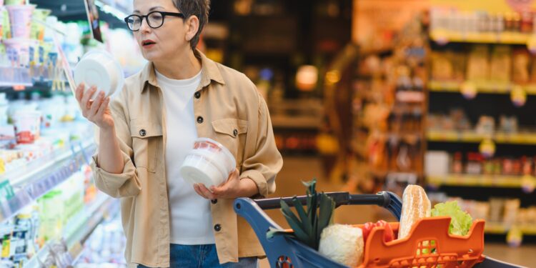 Pessoa analisando diferentes opções de alimentos saudáveis e indulgentes em um supermercado, ilustrando a atenção visual nas escolhas alimentares.